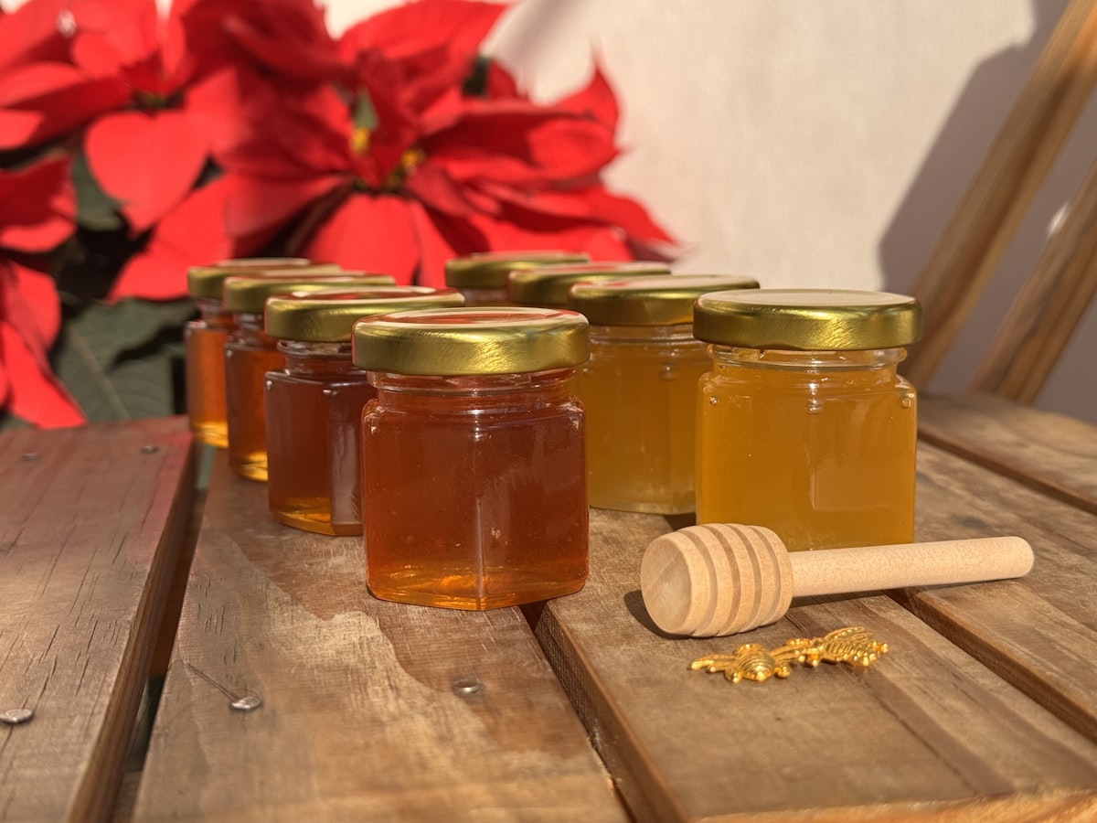 Jars of golden farm honey in the sunlight with a wooden dipper